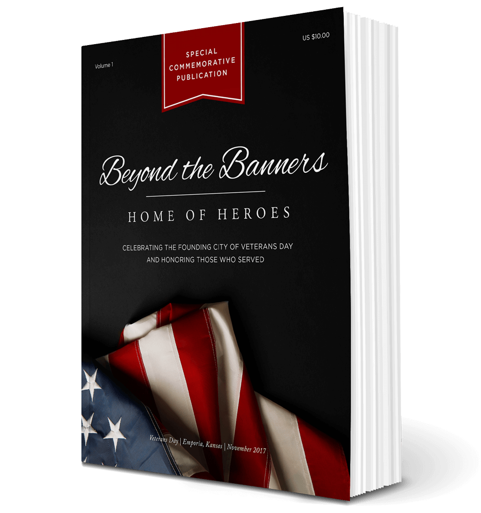 Volume 1 softcover of Beyond the Banners: Home of Heroes Volume 2. The book's cover is black with an american flag placed on the bottom. Text on the top says, "Volume 1. Special Commemorative Publication. US $10.00." Text in the middle says, "Beyond the Banner: Home of Heroes, Celebrating the founding city of Veterans Day honoring those who served." Text on the bottom says, "Veterans Day | Emporia, Kansas | November 2017."